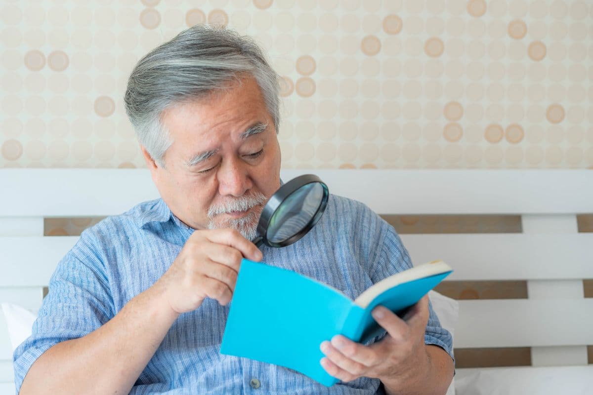 Orang tua membaca buku dengan kaca pembesar karena rabun dekat