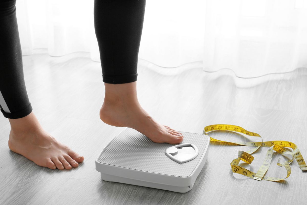 Seorang wanita sedang bersiap menimbang badan menggunakan timbangan lantai