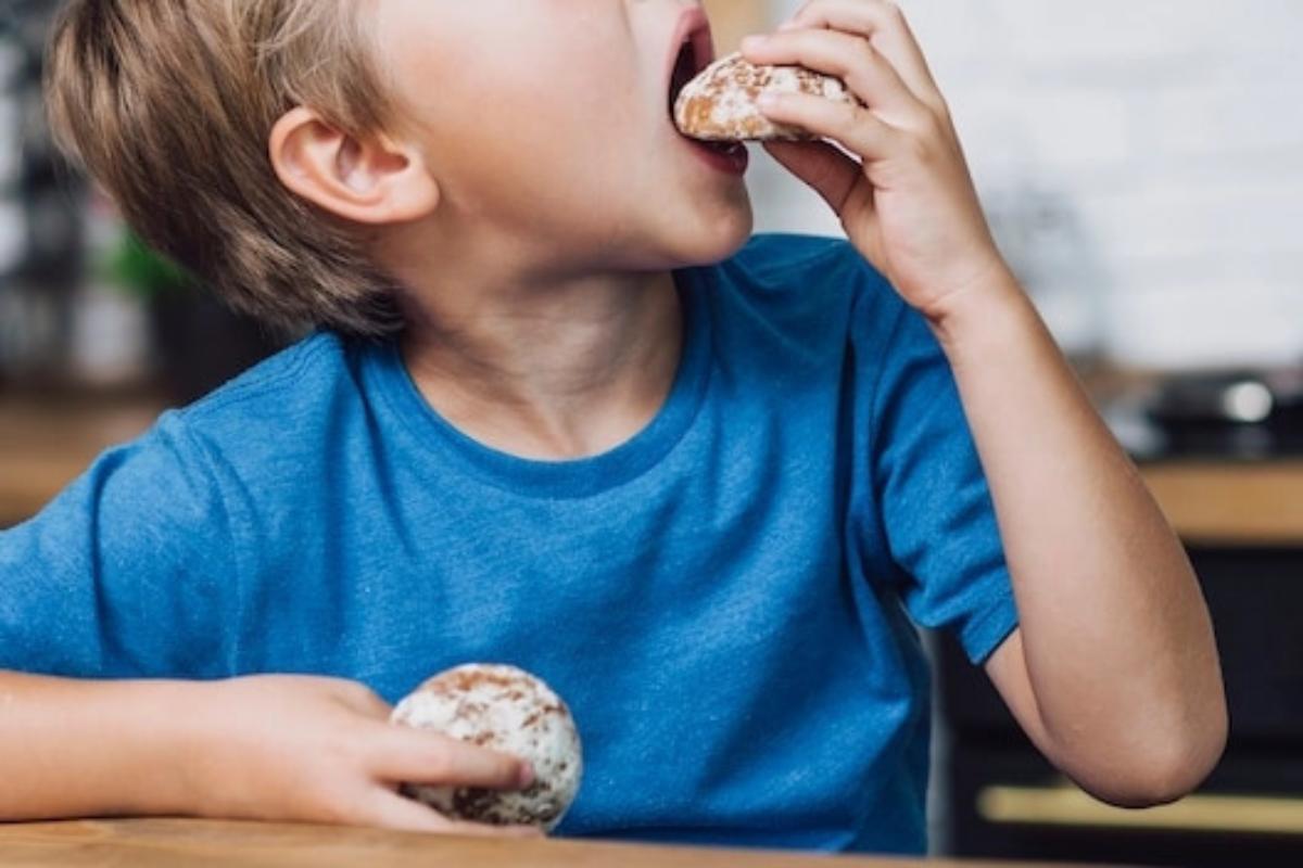 Anak berbaju biru memasukkan kue ke mulutnya
