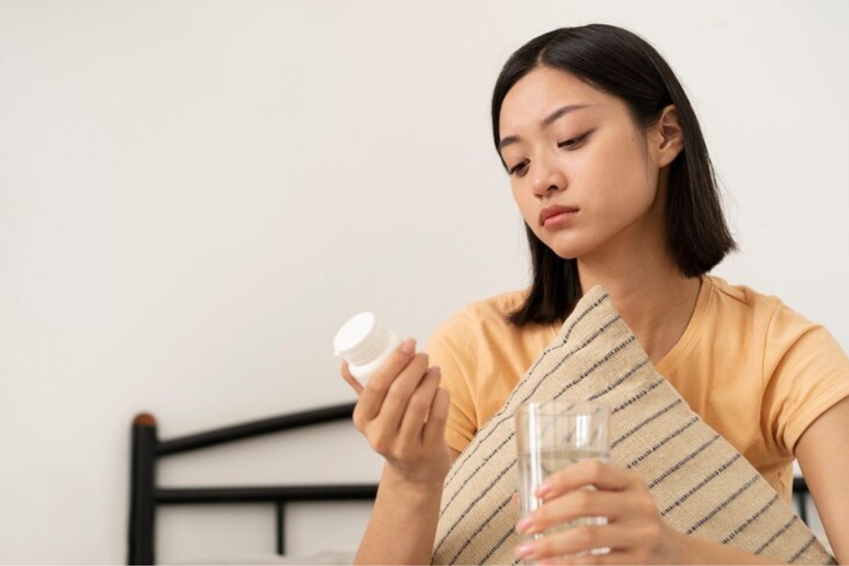 seorang wanita memegang gelas berisi air dan botol suplemen vitamin