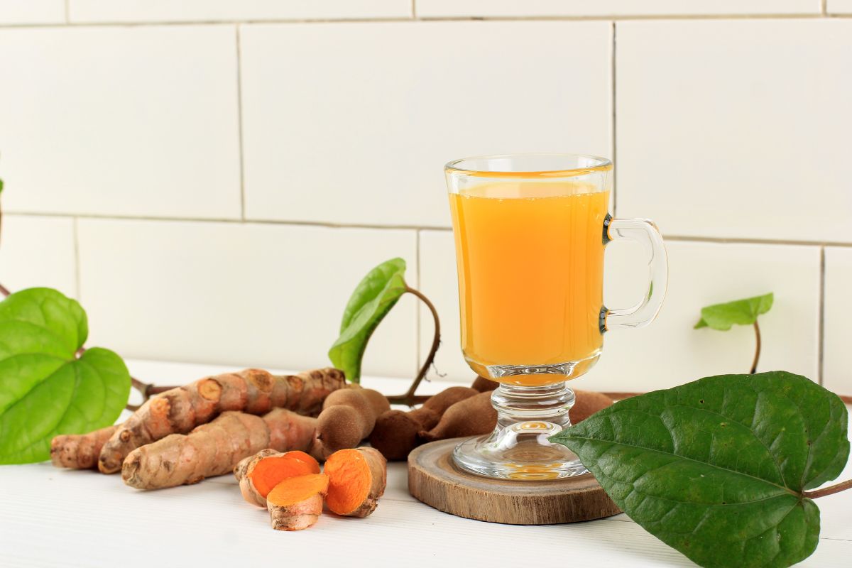 Segelas jamu kunyit dan kunyit segar disekitarnya