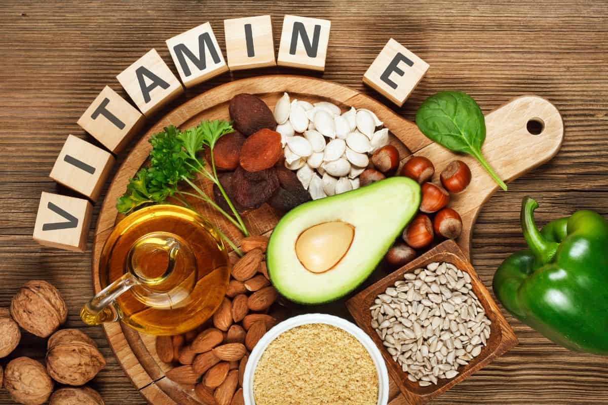 Berbagai makanan sumber vitamin E dan susunan balok kayu bertuliskan "vitamin E"