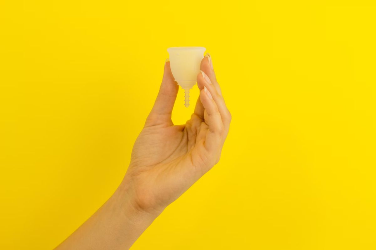 Memegang menstrual cup dengan background kuning